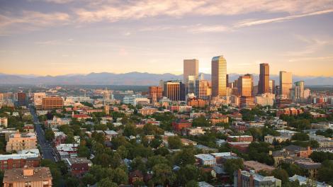 The downtown Denver, Colorado, skyline surrounded by tree-laden neighborhoods and Rocky Mountain views 