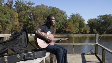 Cedric Burnside 钓鱼间隙在密西西比州杰克逊弹奏吉他 Cedric Burnside 钓鱼间隙在密西西比州杰克逊弹奏吉他
