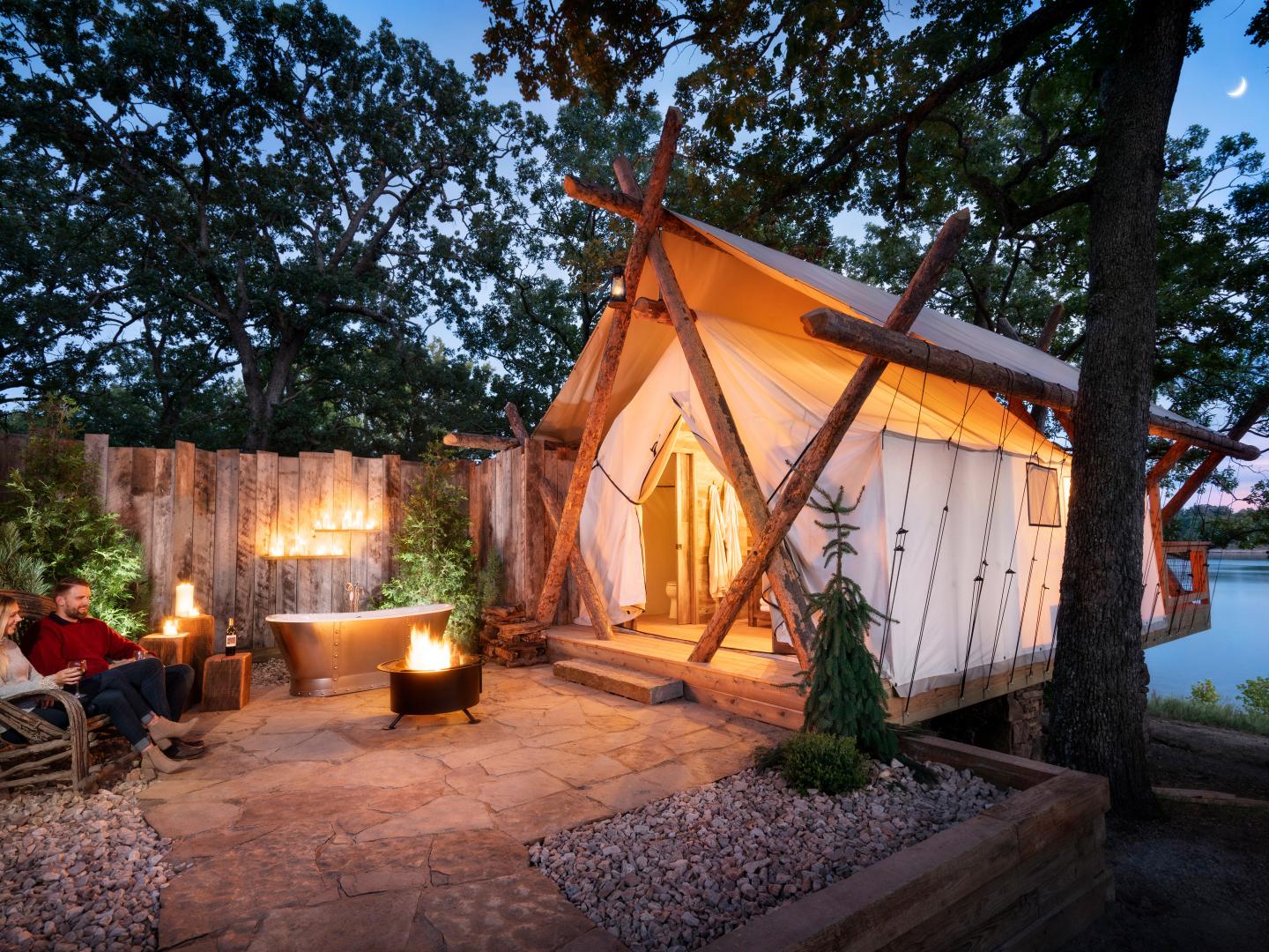 在密苏里州里奇代尔 Big Cedar Lodge 旅馆的长溪营地,一对情侣在篝火和露营帐篷旁放松身心 在密苏里州里奇代尔 Big Cedar Lodge 旅馆的长溪营地,一对情侣在篝火和露营帐篷旁放松身心